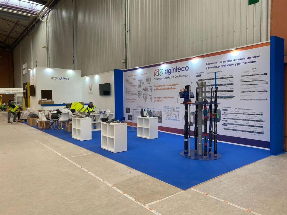 Stand abierto con paneles informativos, mobiliario y suelo azul
