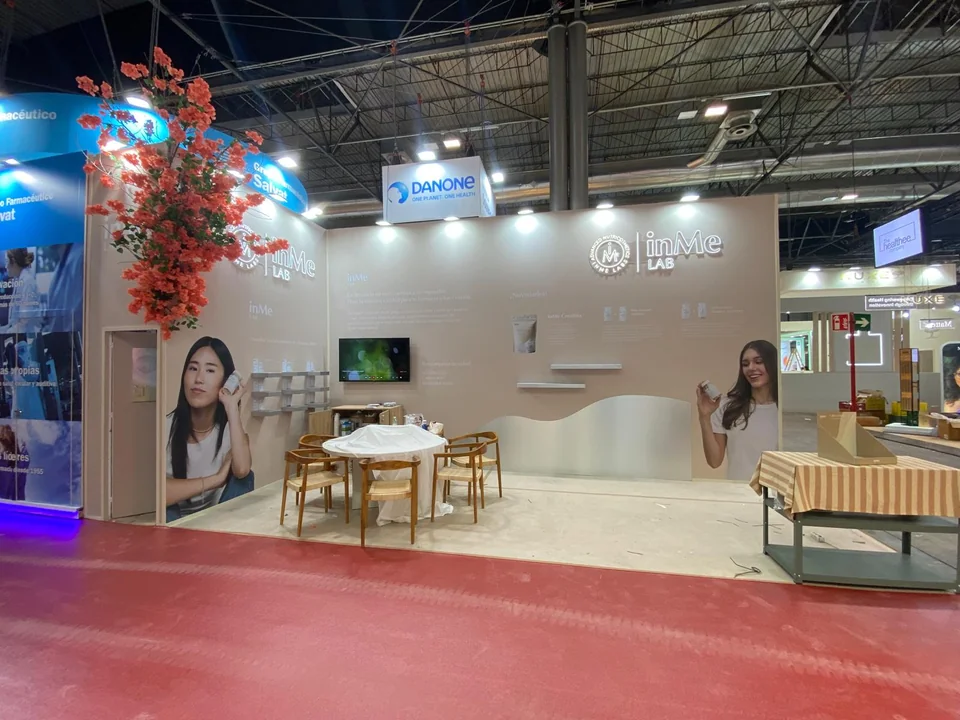 Stand abierto con mesas, asientos y paneles de marca en paredes claras