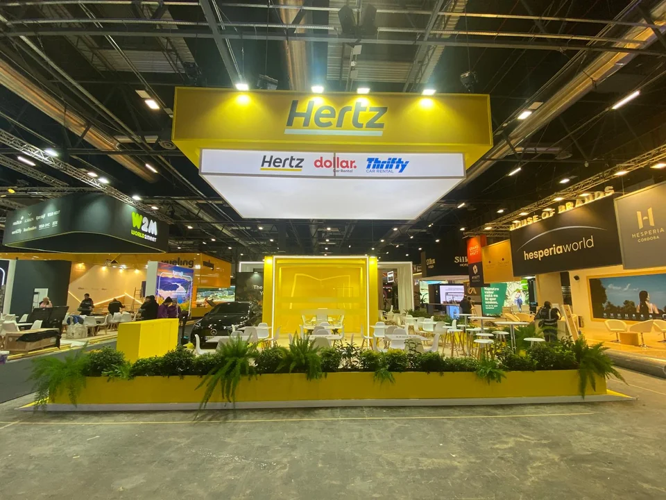 Vista frontal de un stand amarillo con estructura suspendida y zonas de atención
